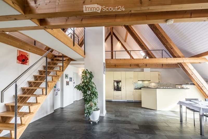Open-plan living and dining area with exposed wooden beams, a staircase leading to an upper level, a potted plant, a modern kitchen with cabinets and a dishwasher, and a dining table with chairs.