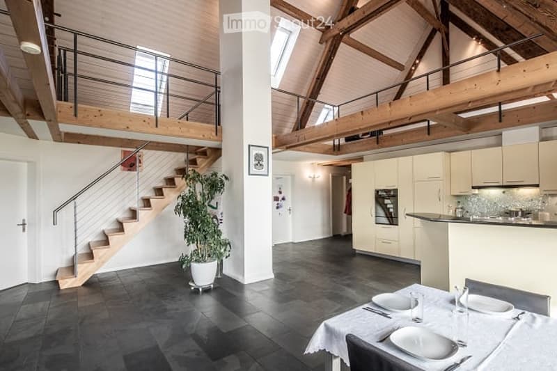Open-plan living and dining area with a staircase leading to an upper level, featuring a large potted plant, a dining table set for four, and a modern kitchen area with cabinets and an oven.