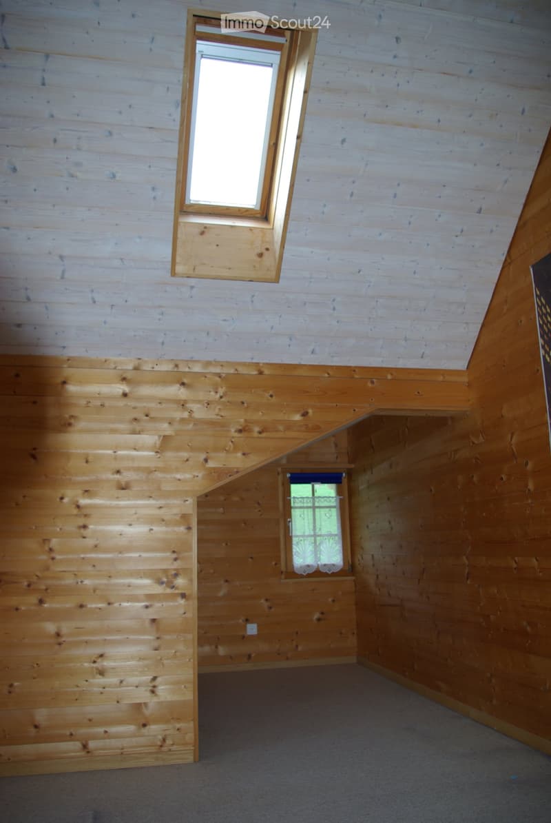 Empty wooden room with exposed beams, two windows, and a built-in shelf. No furniture or equipment present.