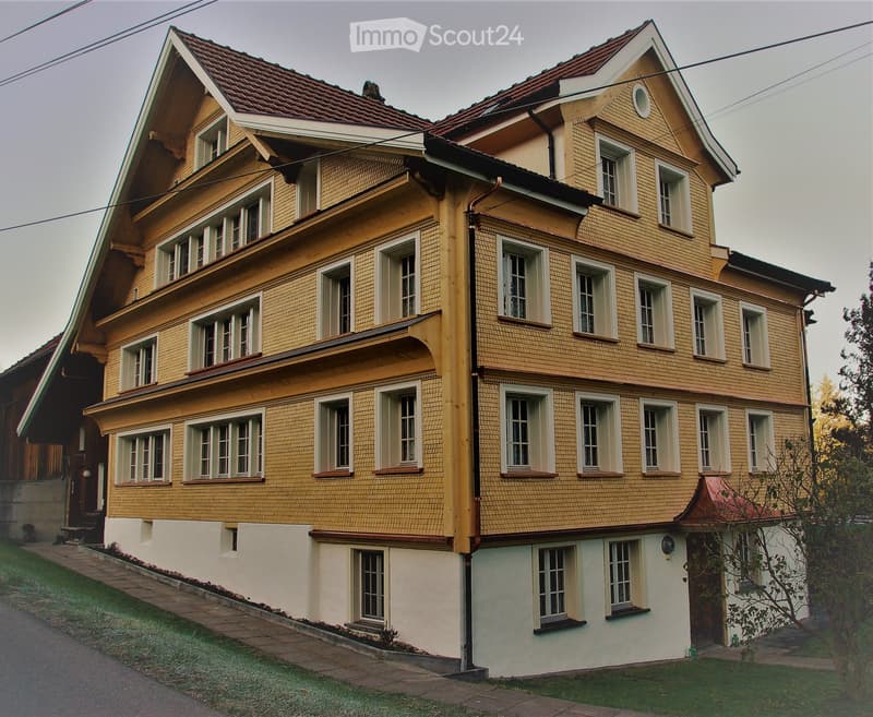 Two-story yellow house with multiple windows, red-tiled roof, and white trim around windows and roofline.