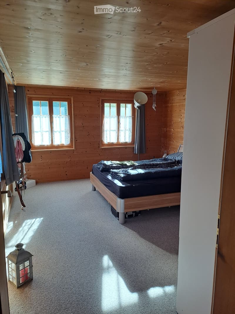 Cozy wooden bedroom with a large bed, wooden walls, large windows with curtains, and a lantern on the floor.