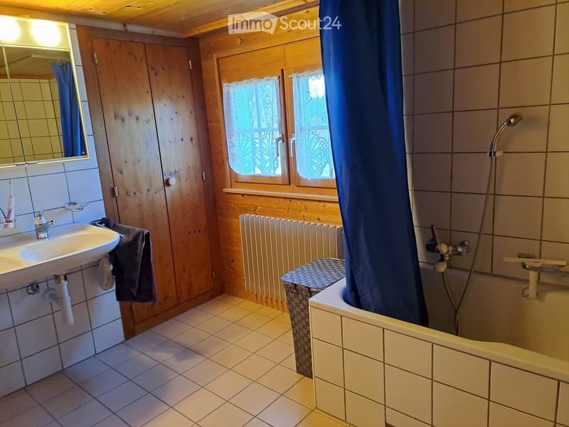 Bathroom with wooden walls, tiled floor, sink, mirror, bathtub with shower, radiator, and a small stool.