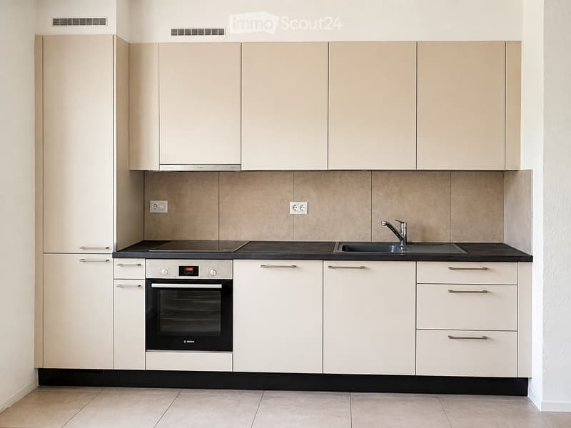 Modern kitchen with light-colored cabinets, black countertops, and stainless steel appliances including an oven and sink.