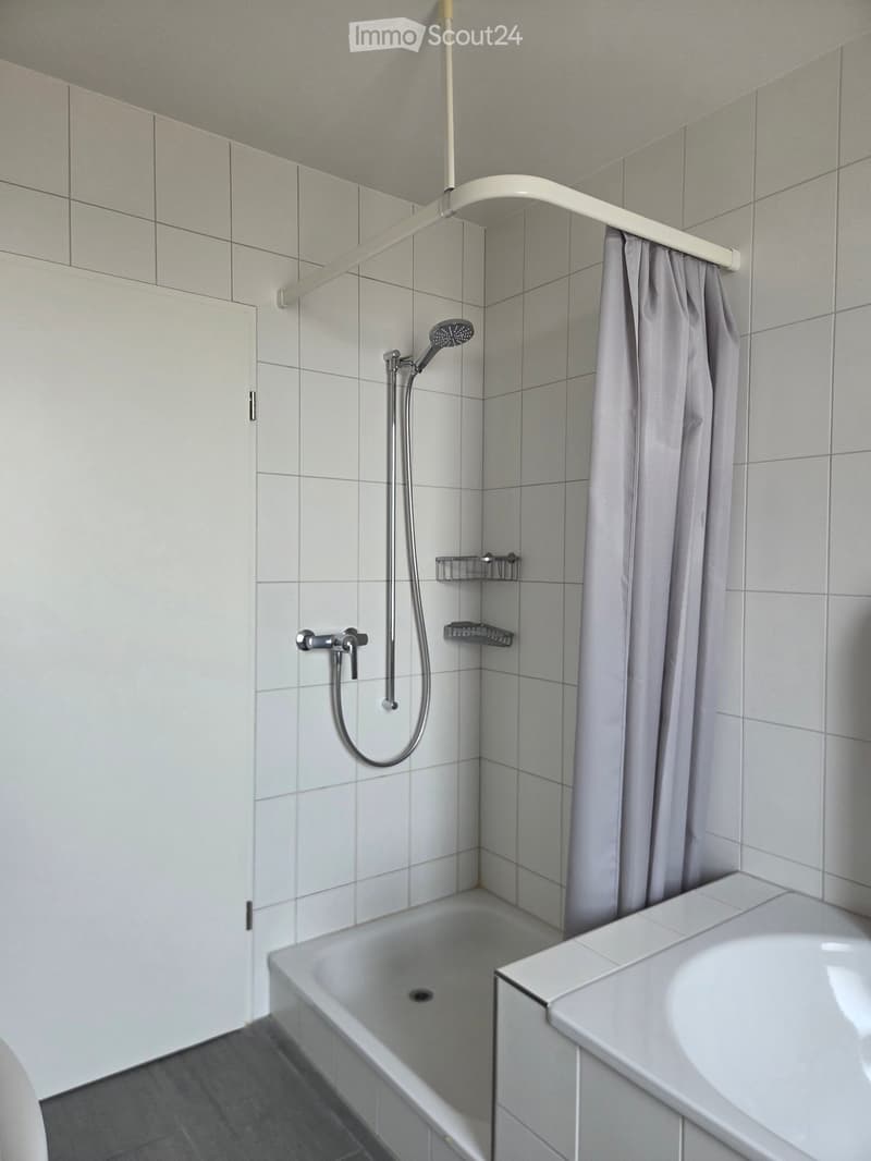 Modern bathroom with a bathtub, showerhead, and a sink. The shower area features a curtain and a shelf for storage.