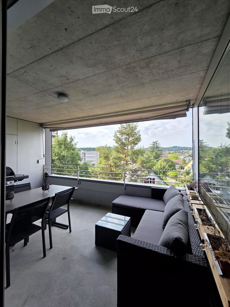 Modern balcony with a view, featuring a sofa, table, chairs, and a small stool.