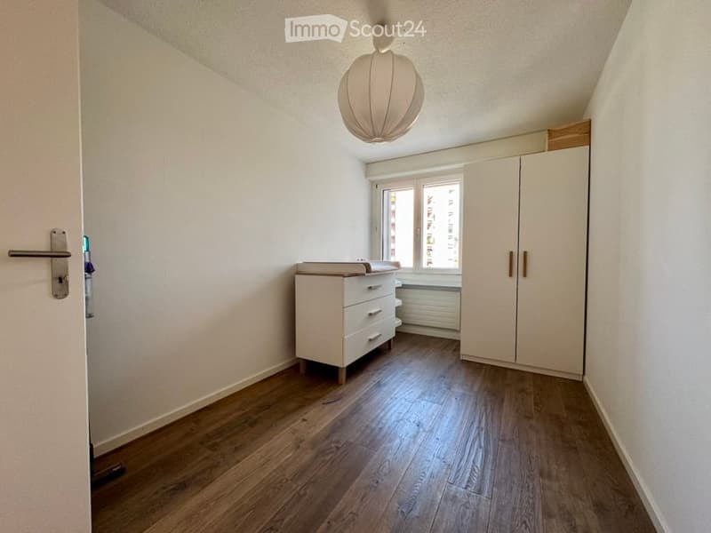 Empty room with wooden flooring, white walls, a window, a door, and a built-in wardrobe.