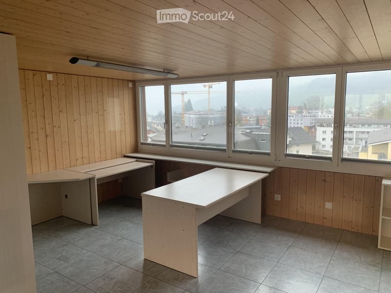 Empty room with wooden walls and ceiling, large windows offering a cityscape view, and several built-in desks.