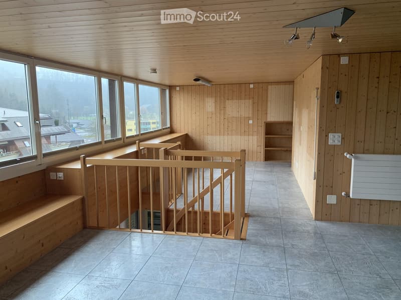Bright hallway with wooden walls and ceiling, large windows, staircase with wooden railing, built-in bench seating, and a small shelf unit.