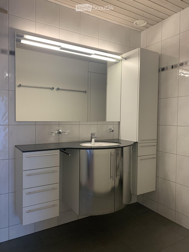Modern bathroom with a white sink, mirror, and cabinets, featuring a sleek design and bright lighting.