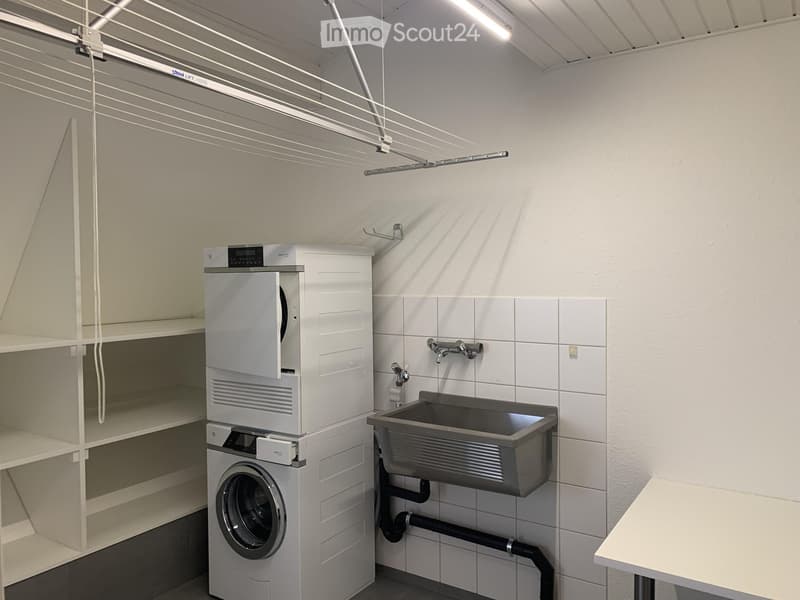Modern bathroom with a washing machine, sink, and faucet, featuring white tiled walls and a drying rack.