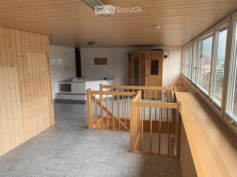 Modern, well-lit room with wooden walls and ceiling, featuring a staircase, a sink area with a mirror, and a wooden sauna.