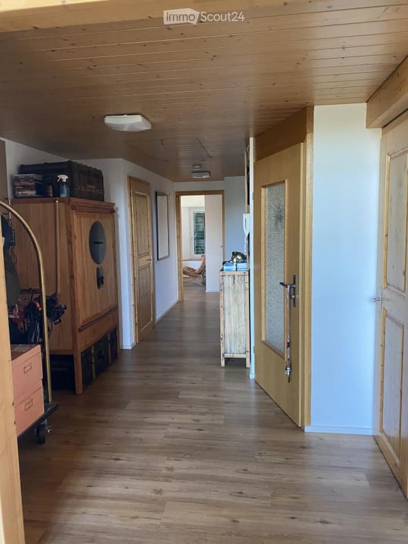 A well-lit hallway with wooden flooring and light-colored walls, featuring several doors and a small table with items on it.