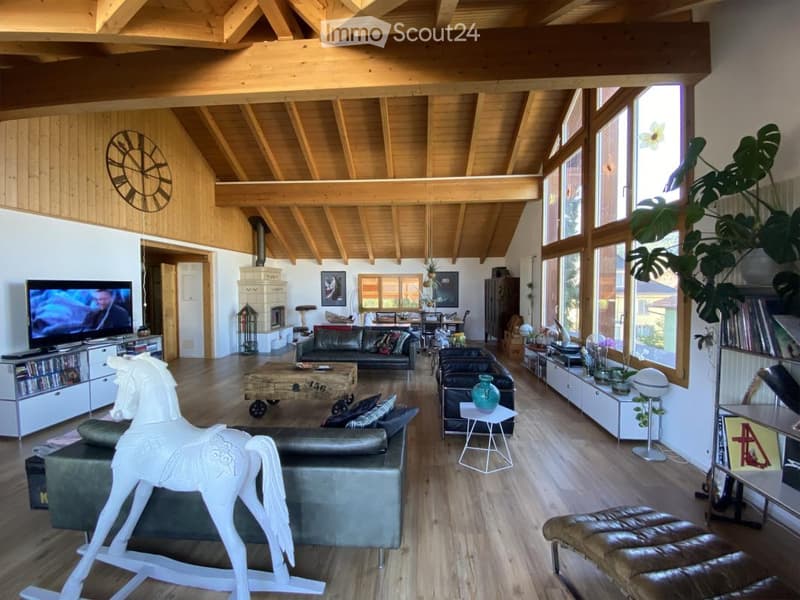 Bright living room with wooden beams, large windows, leather sofas, coffee table, television, decorative rocking horse, and various decorative items.