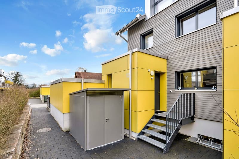 Modern building with yellow and gray exterior, metal staircase, and a gray storage shed.