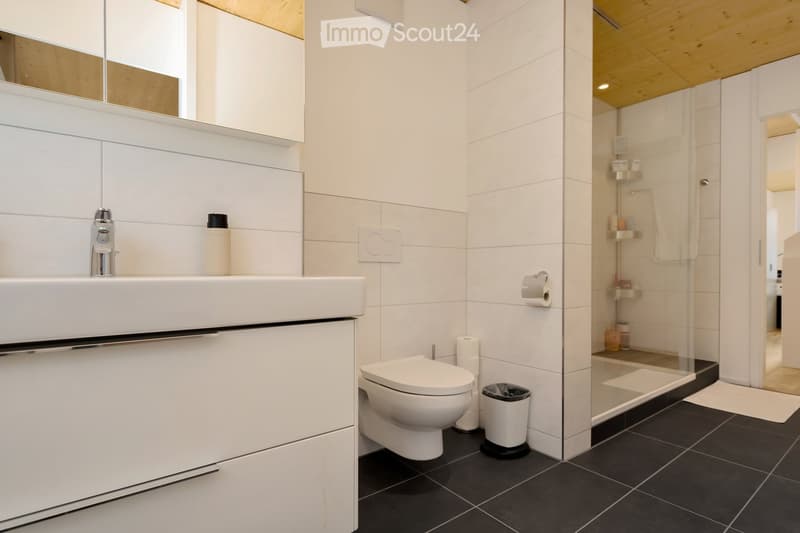 Modern bathroom with white tiles, a white sink, a toilet, and a glass shower enclosure.