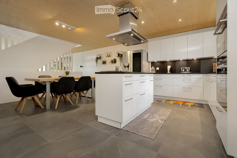 Modern kitchen with white cabinets, gray tiled floor, and a central island. Dining table and chairs are placed nearby.