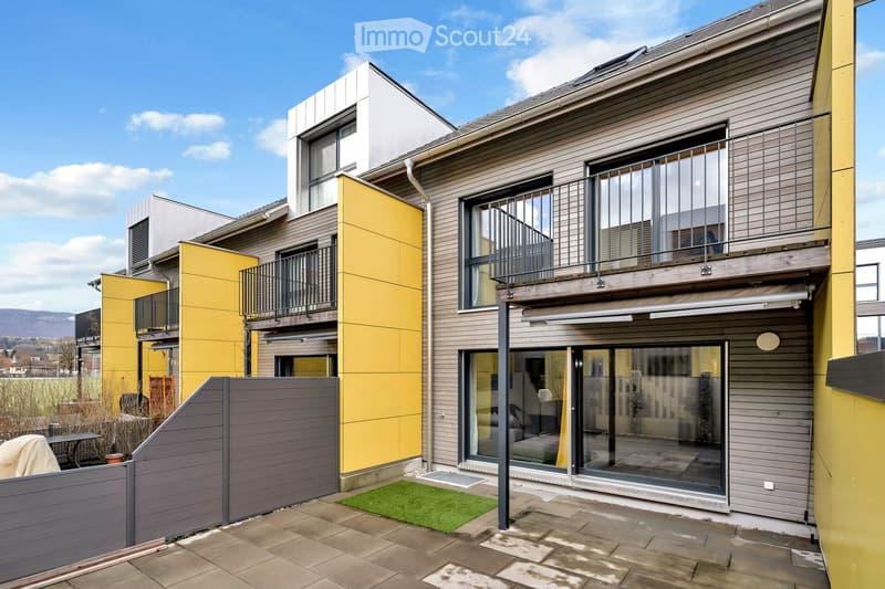 Modern building with yellow and grey exterior, balconies, and a fenced courtyard.