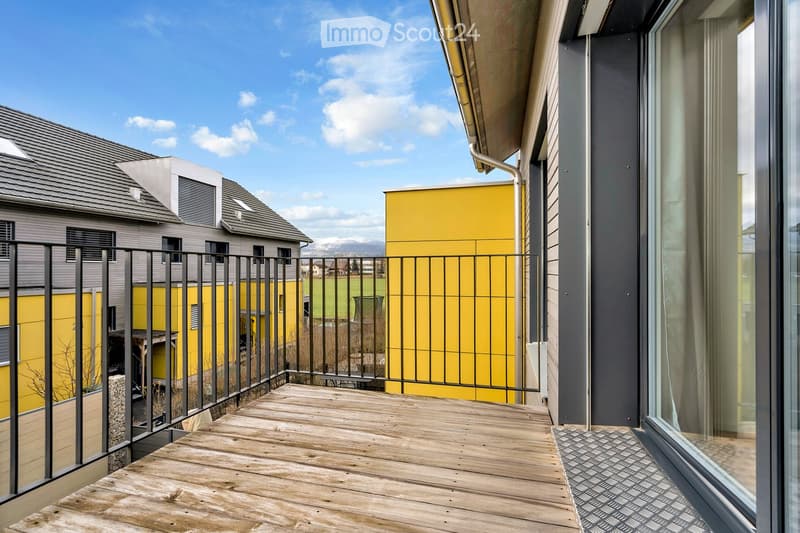 Wooden balcony with black railings, yellow walls, and a view of a grassy field.