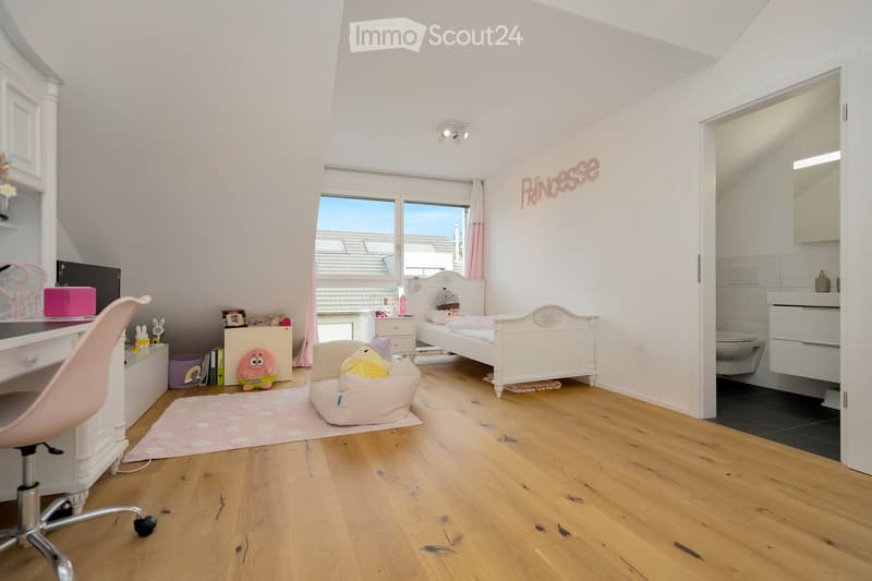 A child's room with a bed, desk, chair, toys, rug, nightstand, lamp, and a small toilet and sink in the bathroom.
