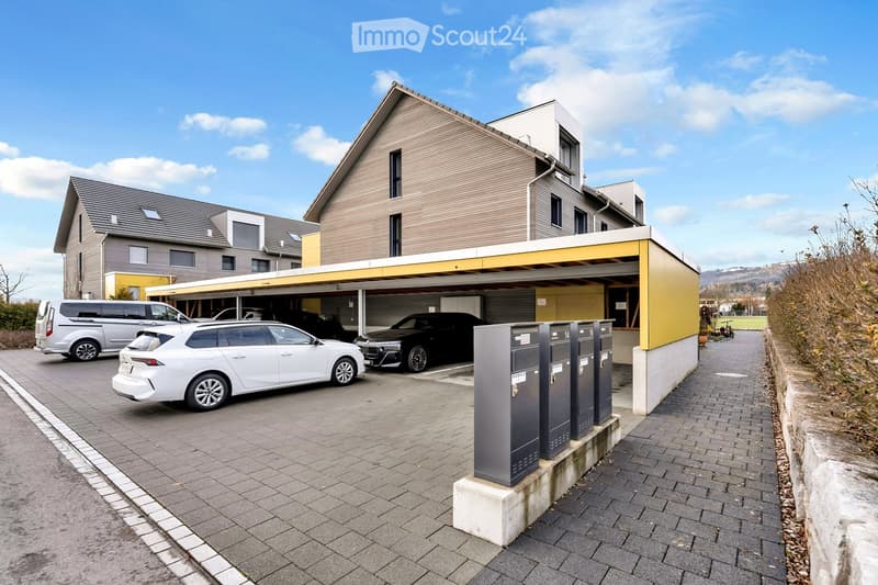 Modern building with a carport, featuring a yellow and brown exterior, and a row of mailboxes.