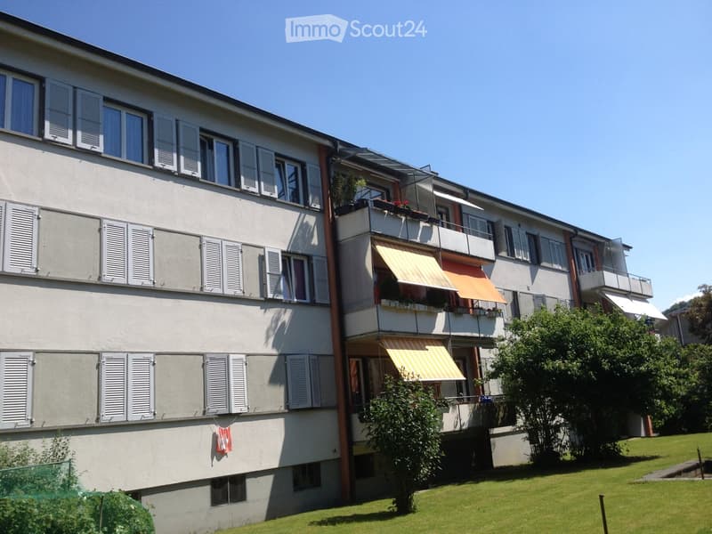 Multi-story residential building with balconies, shutters, and a well-maintained lawn in front.