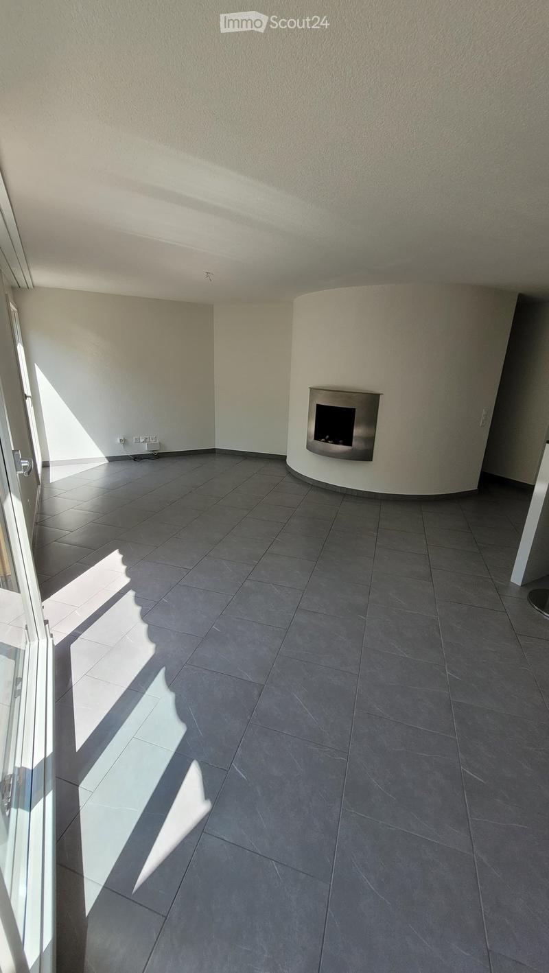 Empty room with grey tiled floor, white walls, and a built-in fireplace. Sunlight streams in from a large window on the left side.