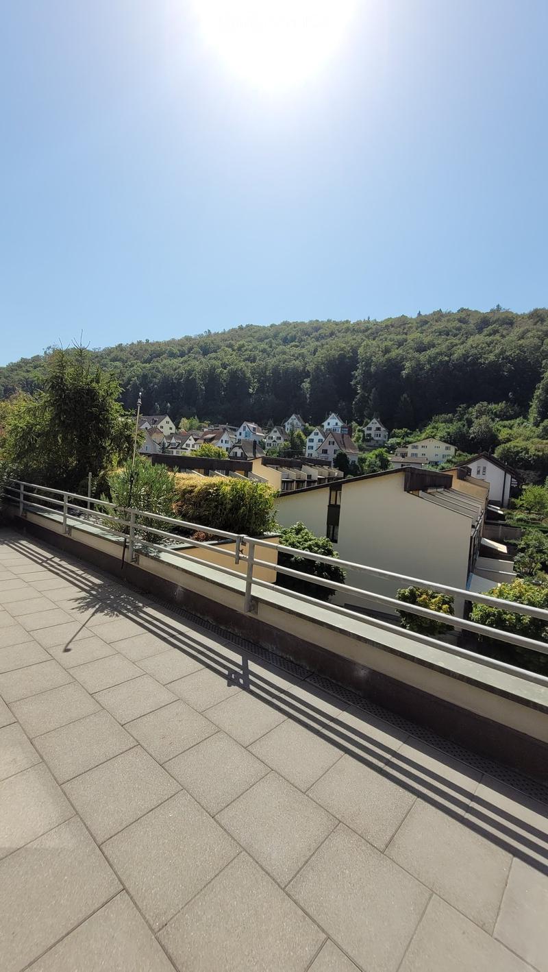 Balcony with tiled floor, metal railing, and scenic view of a town and forested hills in the background.