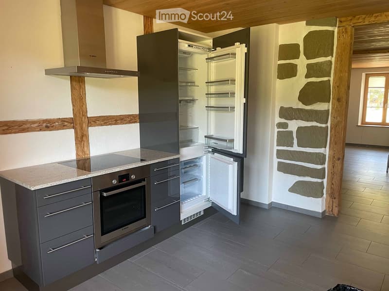 Modern kitchen with dark grey cabinets, stainless steel appliances, and a stone accent wall. Features an open refrigerator, oven, and kitchen island with a granite countertop.