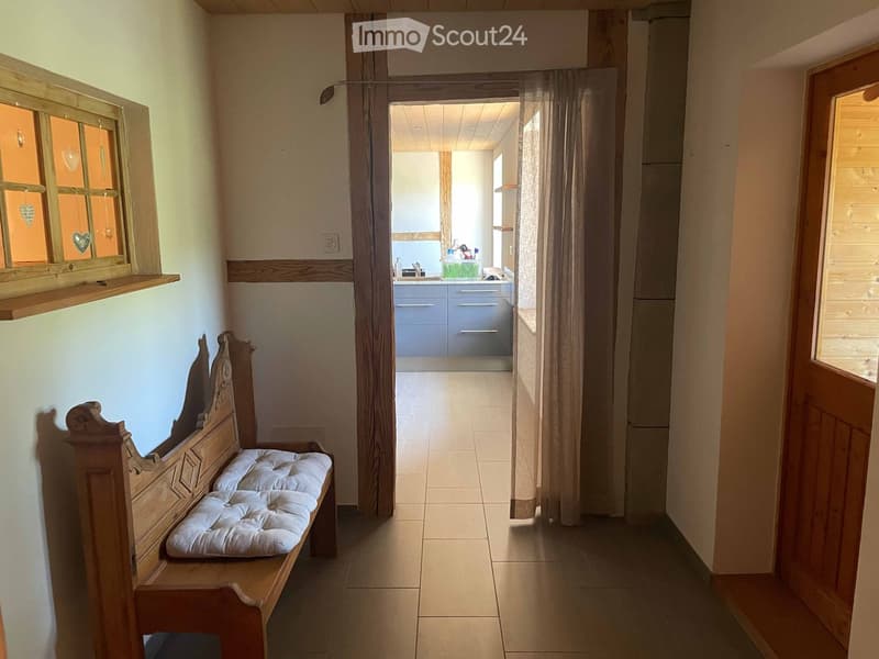 Hallway with wooden bench, white cushion, and view into a kitchen area with cabinets and sink.
