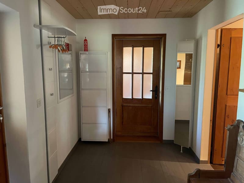 Hallway with tiled floor, wooden door with glass panels, coat rack, and cabinets on either side.