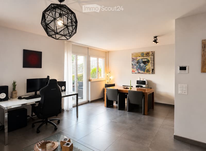 Modern, well-lit room with a desk setup, a dining table, and contemporary decor including a geometric light fixture and artwork.