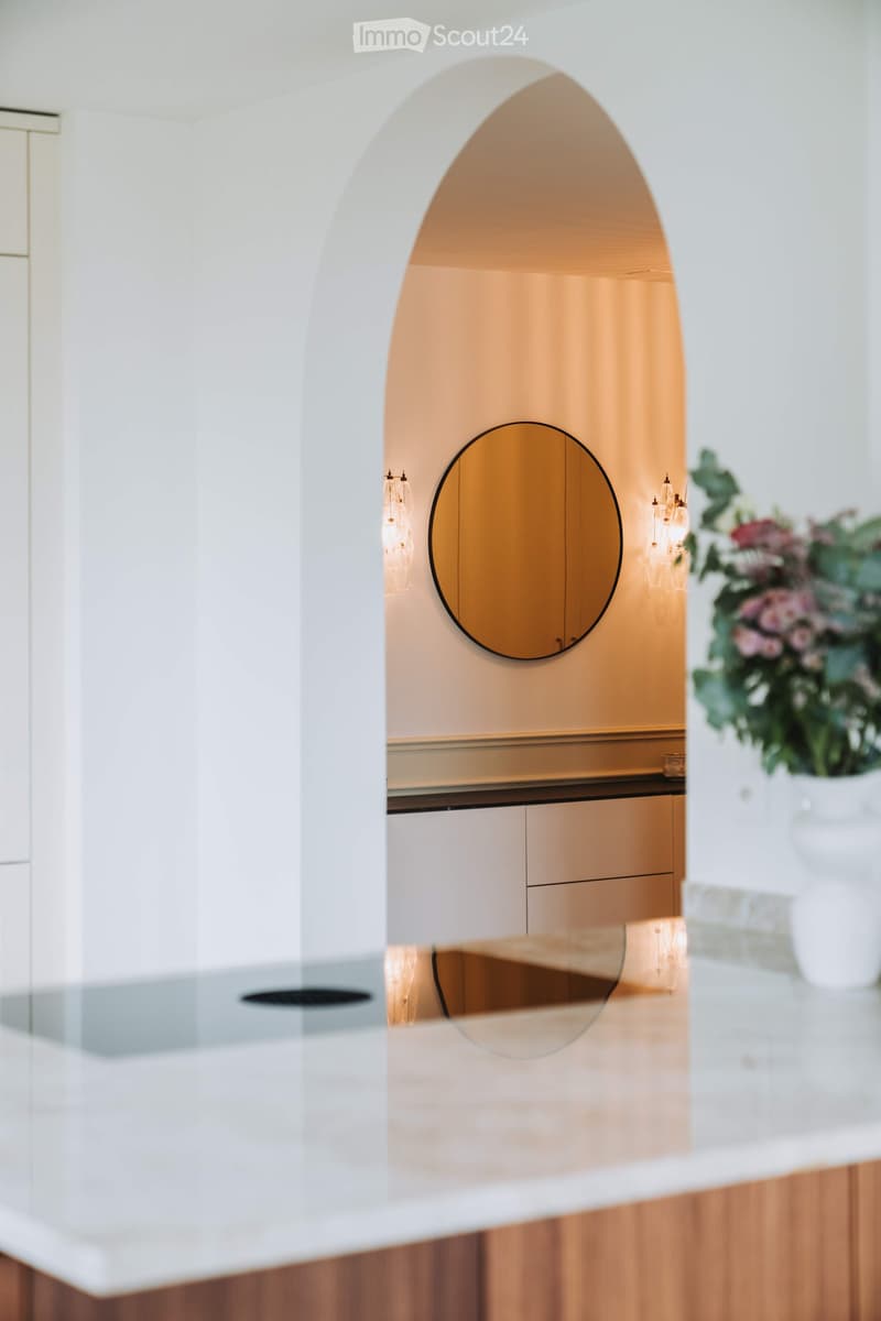 Modern hallway with white walls, wooden flooring, a round mirror, and decorative lighting fixtures.
