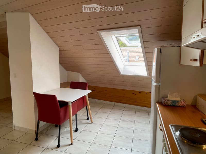 Cozy kitchen with wooden walls and ceiling, white tiled floor, a small dining table with two red chairs, a refrigerator, and a sink with a stove.