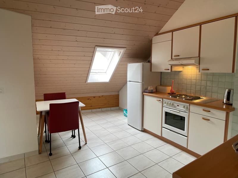 Bright kitchen with wooden walls and ceiling, white cabinets, a refrigerator, stove, and a small dining area with a table and chairs.