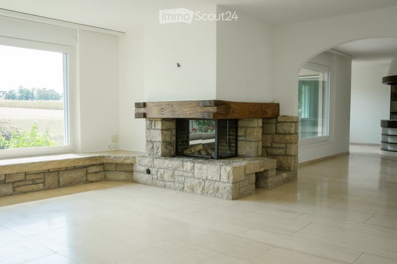 Modern living room with a stone fireplace, large windows, and light wooden flooring.