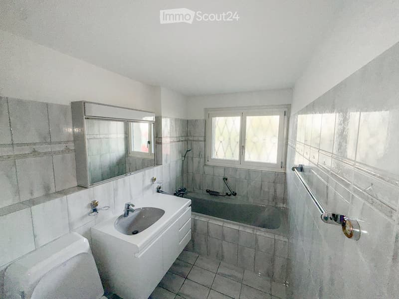 Bathroom with white tiled walls and floor, a sink with a mirror above it, a bathtub with a showerhead, and a toilet.
