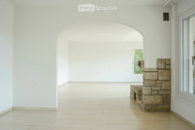 Empty room with white walls, tiled floor, arched doorway, and a stone bench near a window.