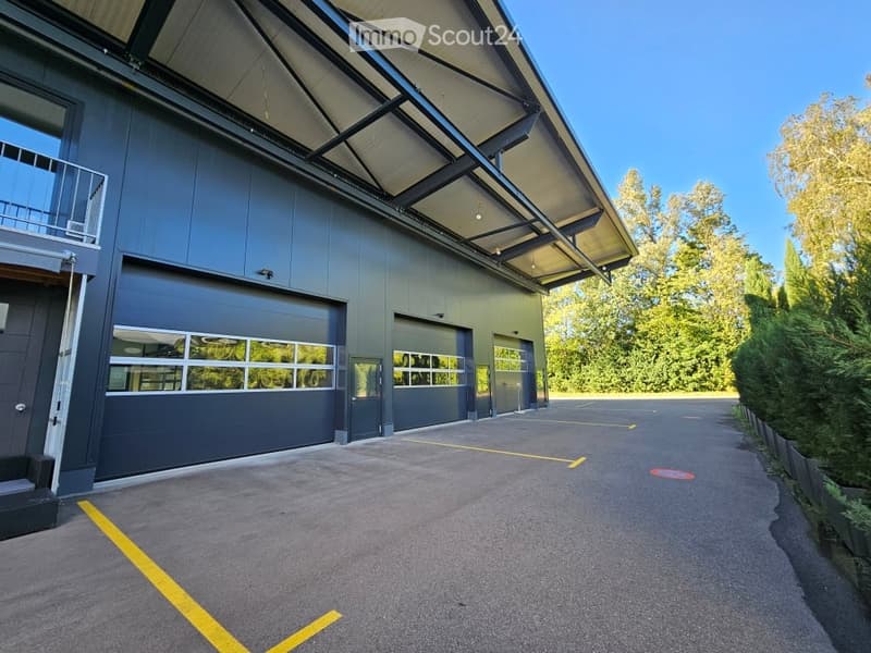 Modern industrial-style building with large garage doors, a covered walkway, and a spacious parking area.
