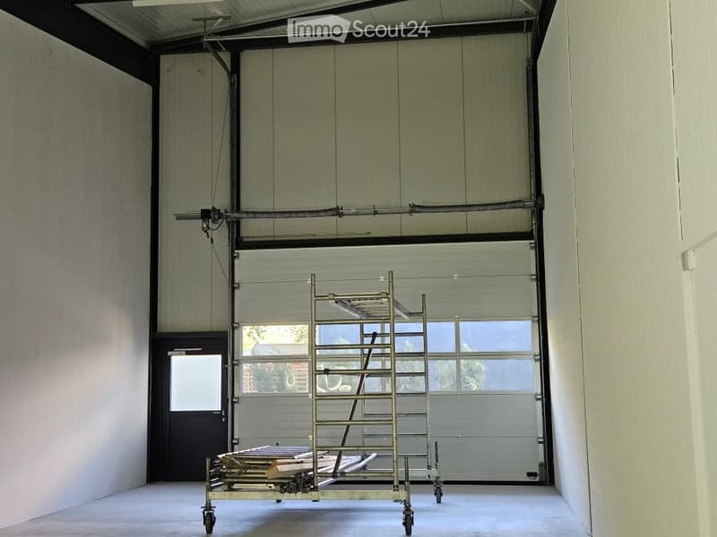 Empty garage with a large roll-up door, a small entryway, and a metal cart with wheels inside.