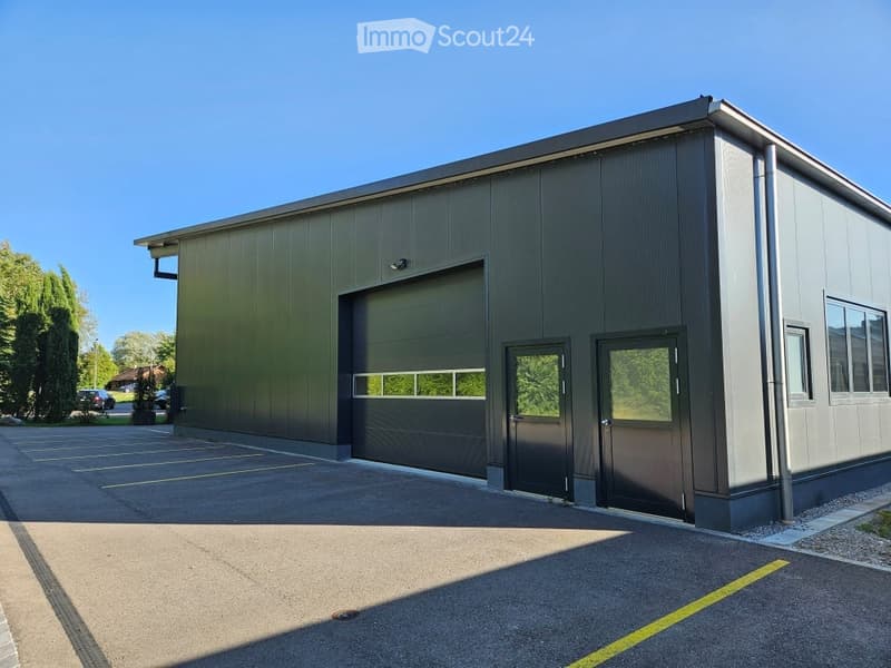 Modern industrial-style building with a large garage door, multiple entry doors, and a clean, contemporary design.