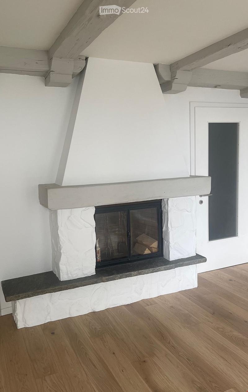 A modern fireplace with a stone surround and wooden mantel, set against white walls and wooden flooring.