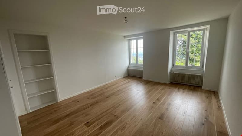 Empty room with wooden flooring, white walls, and large windows allowing natural light. No furniture or equipment present.