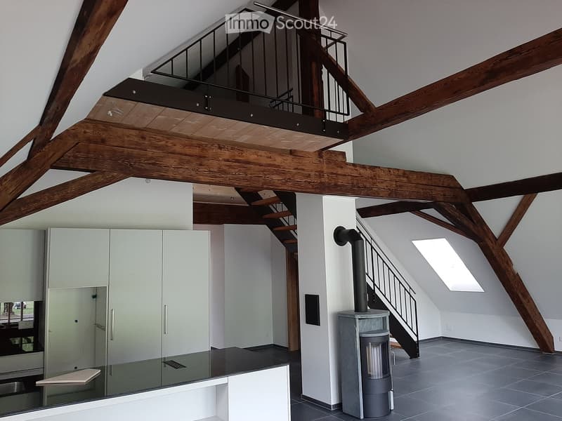 Open-plan living space with exposed wooden beams, a modern staircase leading to an upper level, a built-in cabinet, and a contemporary wood-burning stove.