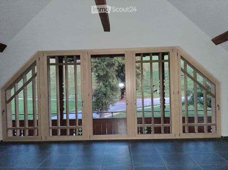 A hallway with large wooden-framed glass doors leading to an outdoor view of a green field and road.