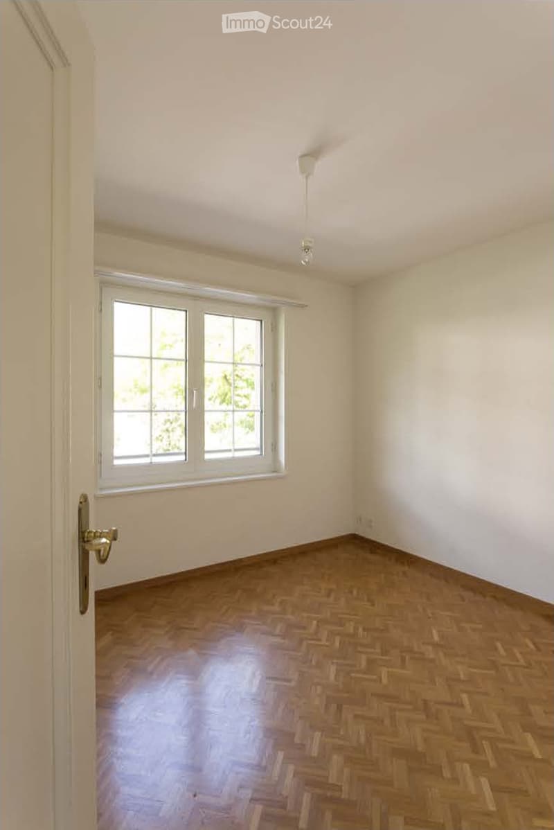 Empty room with wooden herringbone flooring, white walls, and a large window with white frame. No furniture or equipment present.