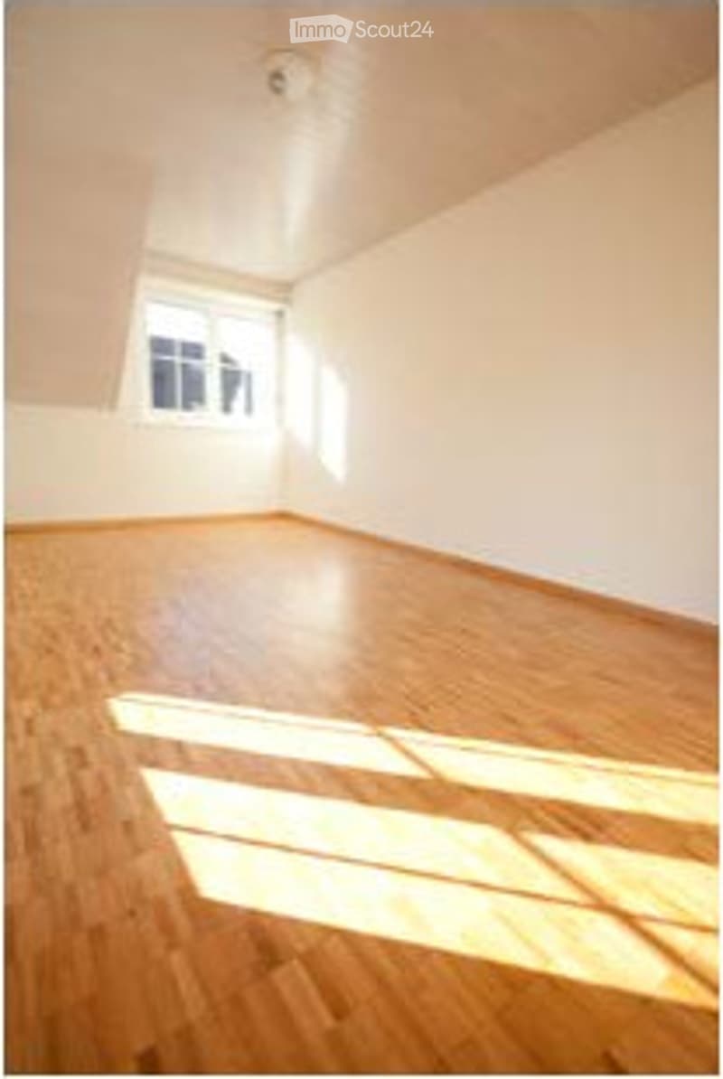 Completely empty room with wooden flooring and white walls, featuring a single window allowing natural light to enter.