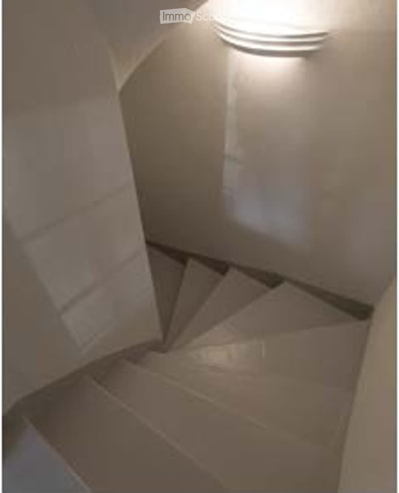 A narrow, carpeted staircase leading upwards, with a single wall-mounted light fixture providing illumination.