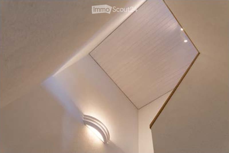A modern hallway with a unique, angular ceiling design featuring built-in LED lighting and a subtle curved wall accent.