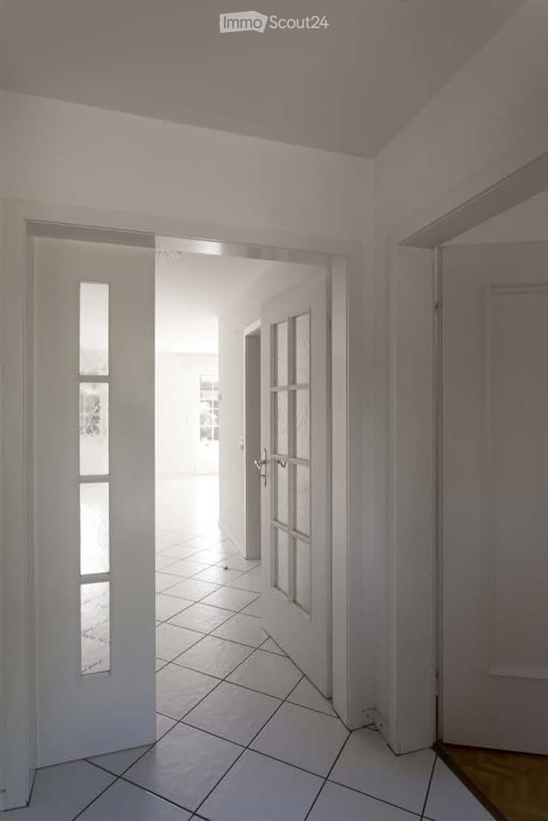 Empty hallway with white tiled flooring, white walls, and a door leading to another room.