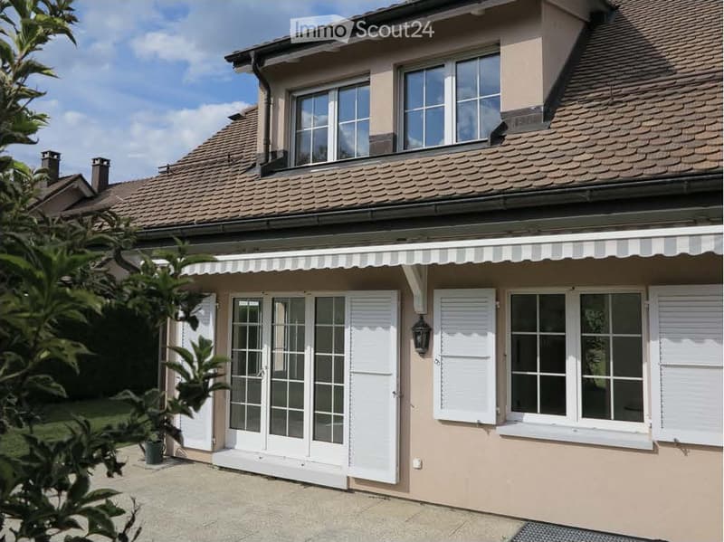 Two-story house with beige siding, tiled roof, multiple windows, and a covered entrance area with white shutters.